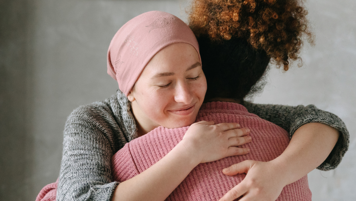 two women hugging, we see the face of one woman, while the second is facing away.