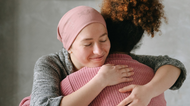 two women hugging, we see the face of one woman, while the second is facing away.